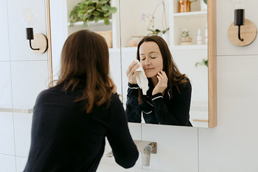 A woman washing her face at a mirror with a face cloth.