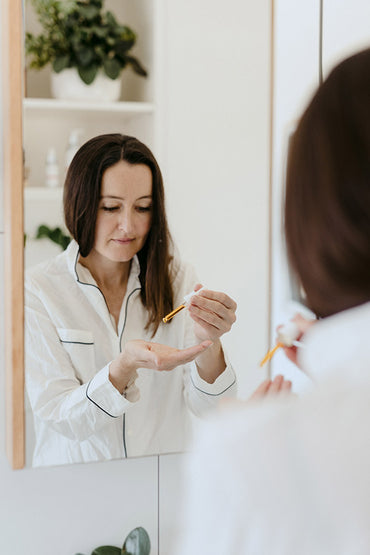 A reflection of a woman in a mirror holding a serum skin care product.