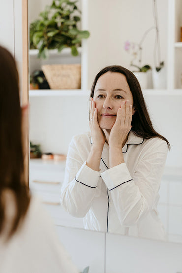 A reflection of a woman in a mirror applying a skin care product to her face.