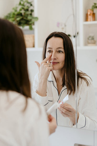 A woman applying a skin care product beneath her eyes.