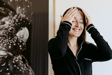 A smiling woman applying a skin care product to her face.