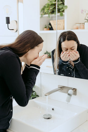 A woman washing an exfoliant & mask skin care product off her face.