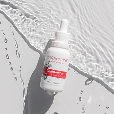 A brightening eye and skin serum skin care product laying on a surface with water behind it.