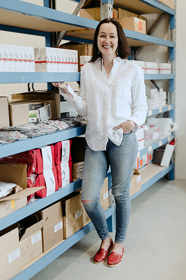 A woman standing in a warehouse beside some brightening eye and skin serum skin care products.