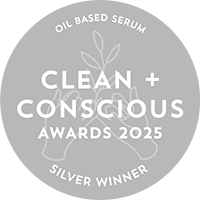 A circular gray badge with white text reading 'OIL BASED SERUM', 'CLEAN + CONSCIOUS AWARDS 2025', and 'SILVER WINNER', plus a simple leaf illustration in the center.