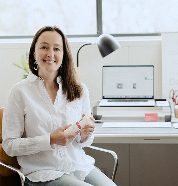 A woman sitting in an office holding an Australian skin care product.