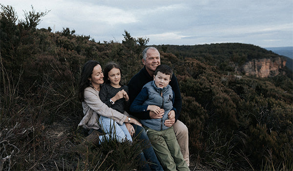 A family sitting in nature, surrounded by trees and mountains.
