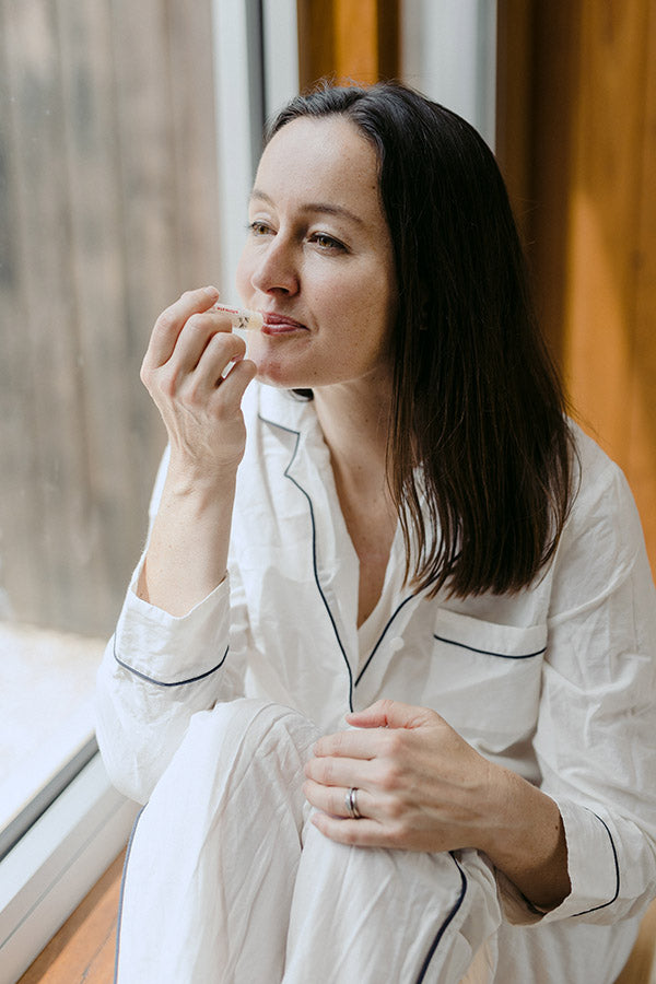 A woman sitting down applying a lip balm to her lips.