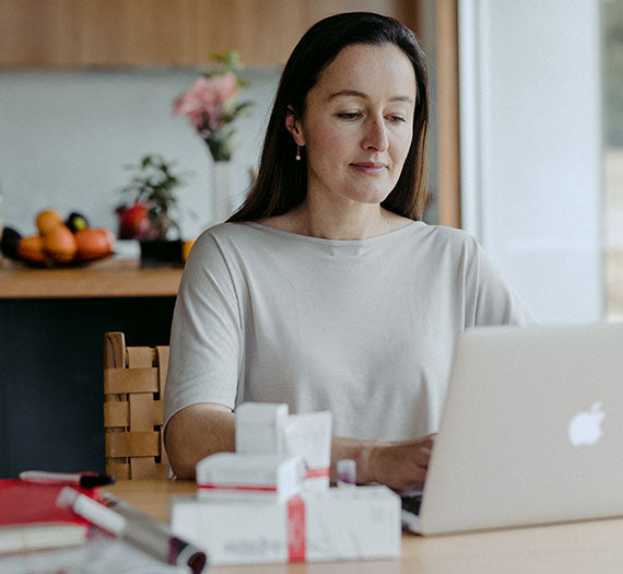 A woman working at a laptop with organic skin care products in the foreground.