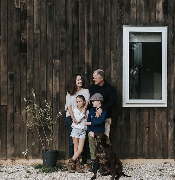 A family standing in front of a house, with a dog sitting in front of the four people.