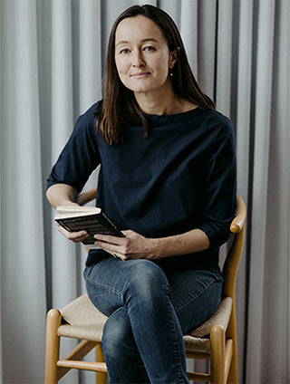 A professional woman sitting at a chair with a book in her hand.