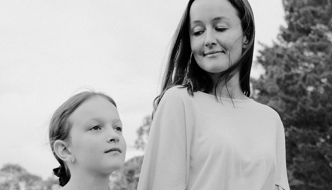 Black and white photograph of a woman and a young girl outdoors, with the woman wearing a light-colored long-sleeve top and the girl looking upward.