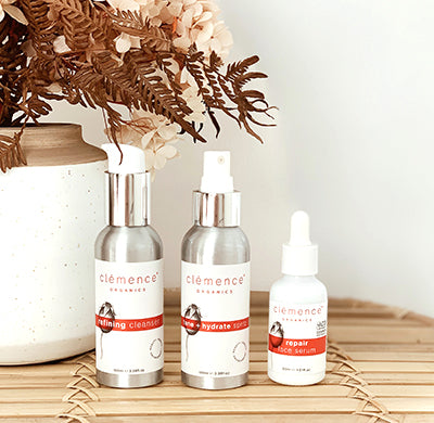 Three organic skincare products, against a white background with dried floral elements, that have been developed for the treatment of Acne.